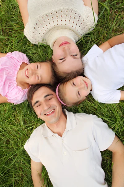 Родители с детьми, лежащими на траве, вид сверху, голова к голове — стоковое фото