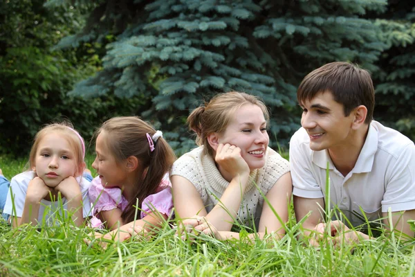 Семья из четырех человек лежит на траве и смотрит друг на друга — стоковое фото