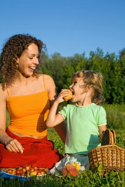 Красивая маленькая девочка и молодые женщины едят фрукты на пикнике — стоковое фото