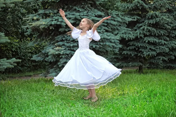 Mädchen in weißem Kleid tanzt mit erhobenen Händen auf Rasen — Stockfoto