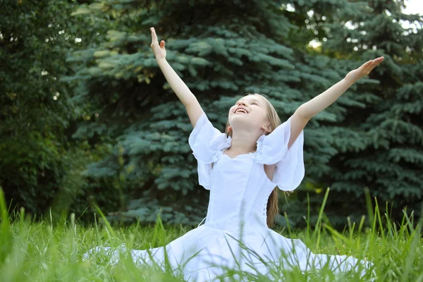 Girl in white dress sits on lawn with lifted hands — Stock Photo, Image