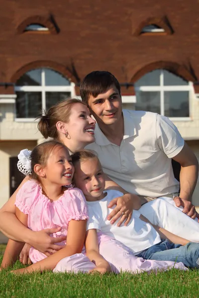 Familie van vier zit op gras tegen huis — Stockfoto