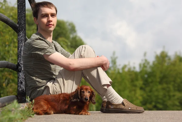 Νεαρός άνδρας και του είδος γερμανικού κυνηγετικού σκύλου κάθεται εξωτερική το καλοκαίρι — Φωτογραφία Αρχείου