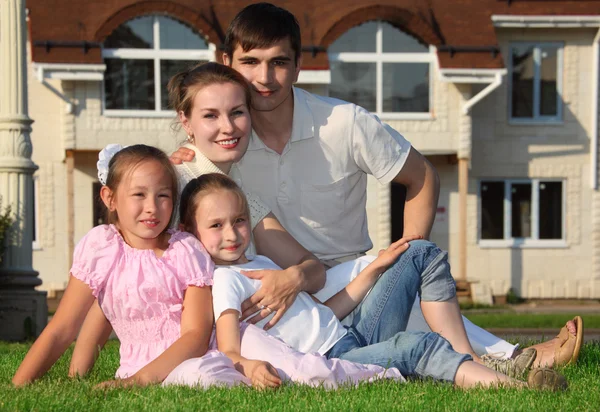 Família de quatro senta-se na grama contra casa — Fotografia de Stock