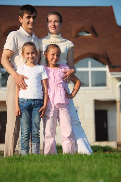 Семья из четырех стоит на траве против дома — стоковое фото