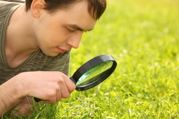 Young man looks through magnifier — Stock Photo, Image