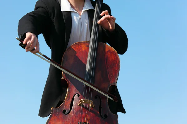 Музыкант крупным планом играет на виолончели против неба — стоковое фото