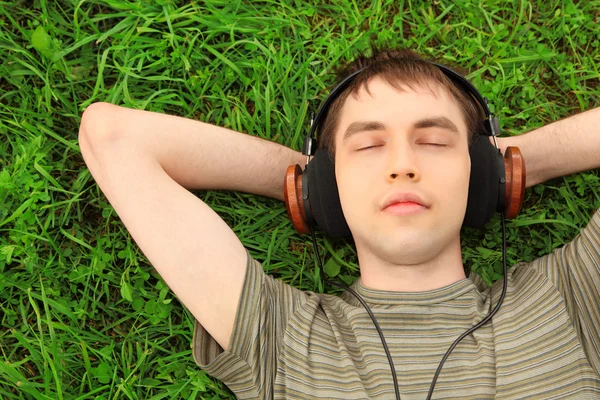 Tonåring ligger på gräset i hörlurar — Stockfoto