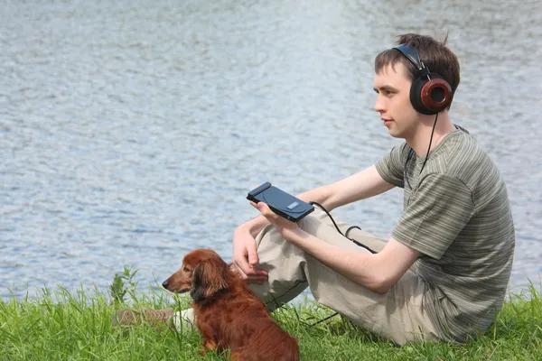 Joven liistens música en auriculares se sienta en la hierba con su da —  Fotos de Stock