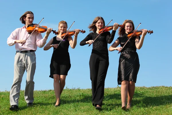 Four musicians go and playing violins against sky, front view — Stock Photo, Image