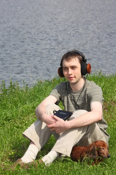 Joven liistens música en auriculares se sienta en la hierba con su da —  Fotos de Stock