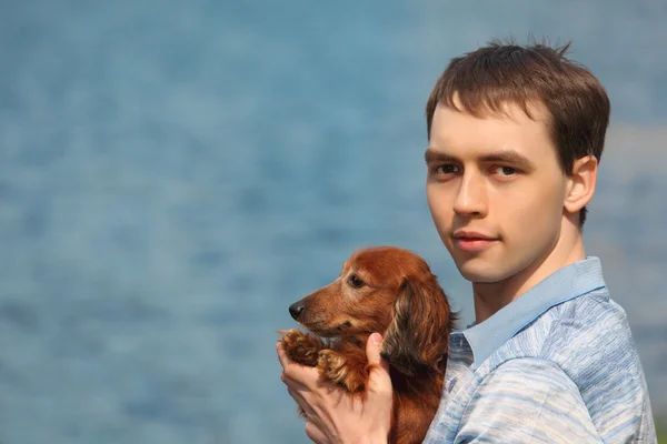 年轻的男人和他可爱的腊肠狗特写反对水 — 图库照片