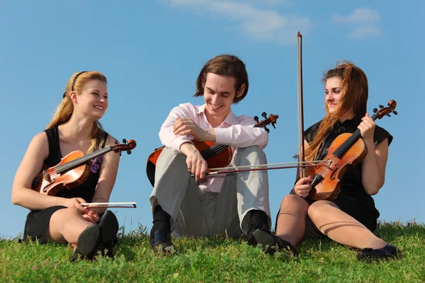 Three violinists sit on grass against sky — Stock Photo, Image