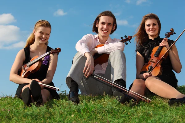 Trois violonistes assis sur l'herbe contre le ciel — Photo