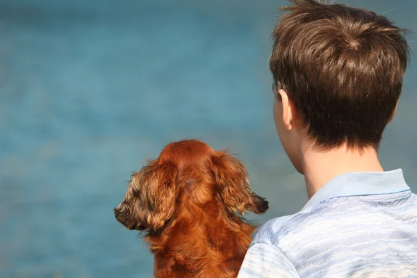 Joven y su perro salchicha desde atrás al aire libre contra el agua — Foto de Stock