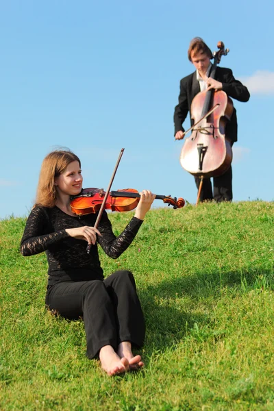 Violinista e violoncelista jogar na grama contra o céu — Fotografia de Stock