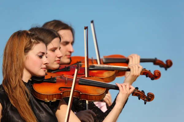 Трио скрипачей играет против неба — стоковое фото