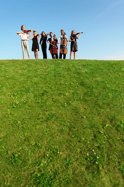 Group of musicians play violins on hill against sky — Stock Photo, Image