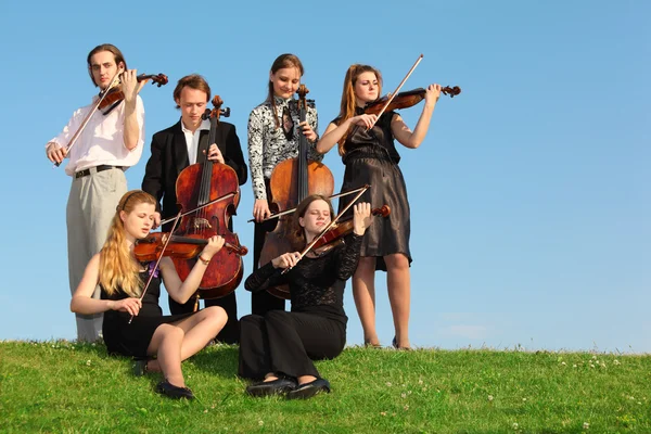 Group of violinists play on grass against sky — Stock Photo, Image