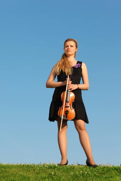 Dziewczyna z skrzypce stoi na trawie przed niebo — Zdjęcie stockowe