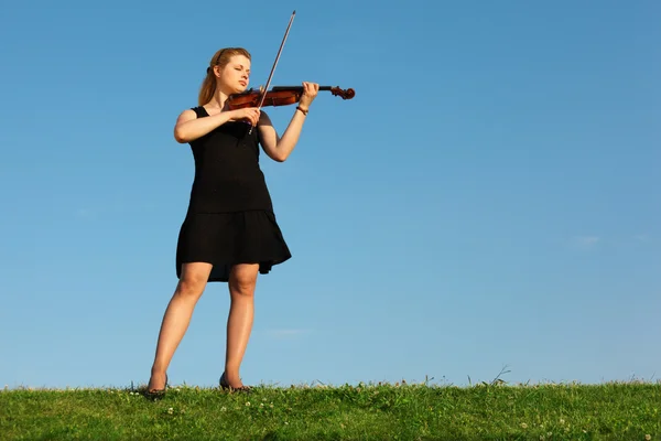 Mädchen steht auf Gras und spielt Geige gegen den Himmel — Stockfoto
