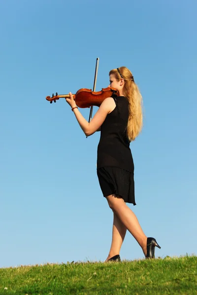 Дівчина стоїть на траві і грає на скрипці проти неба — стокове фото
