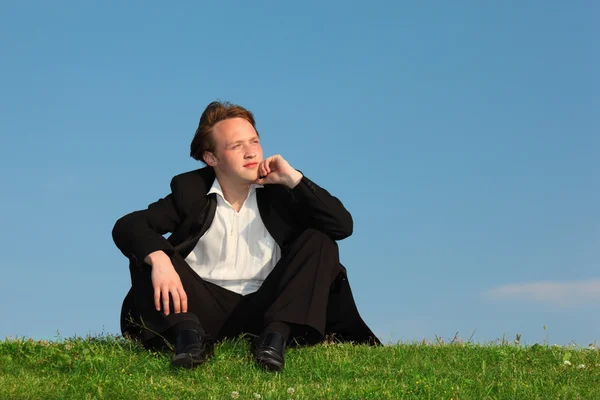 Joven se sienta en el prado contra el cielo — Foto de Stock