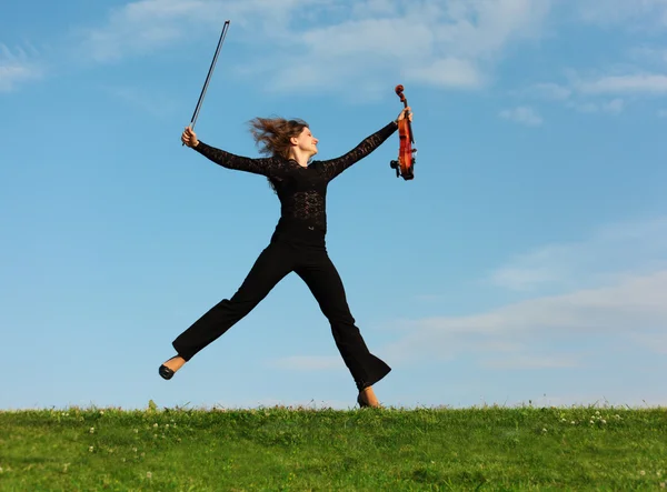 草空を背景にバイオリンの女の子をジャンプします。 — ストック写真