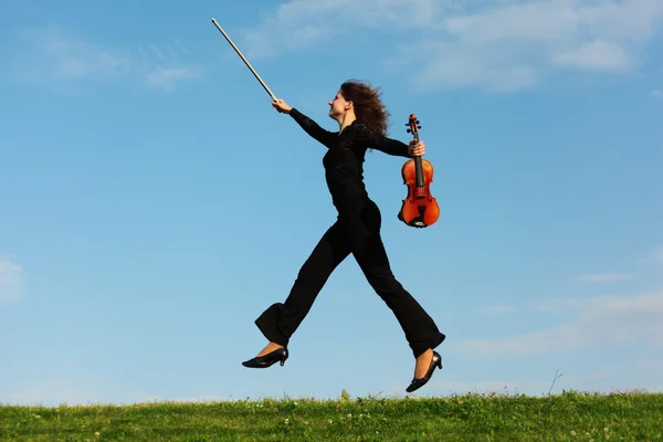 Дівчина зі стрибками зі скрипкою на траві проти неба — стокове фото