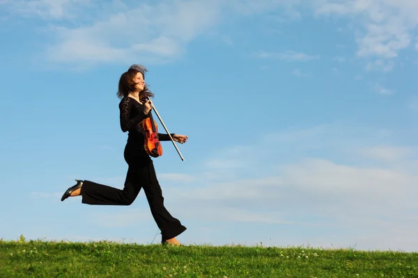 Mädchen mit Geige läuft auf Gras gegen den Himmel, Seitenansicht — Stockfoto