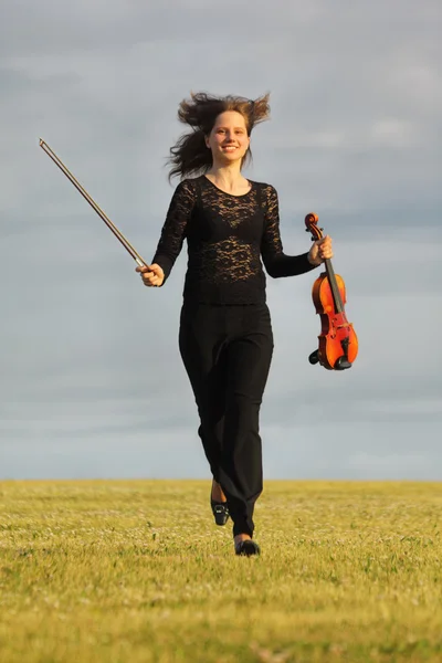 Menina com violino corre na grama contra o céu, vista frontal — Fotografia de Stock