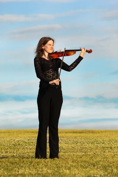 Girl stands on grass and plays violin against sky — Stock Photo, Image