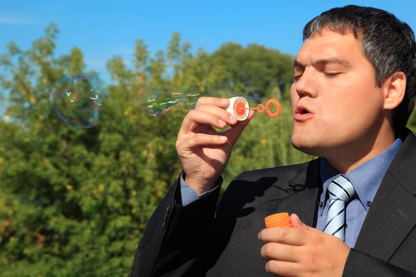 Empresário sopra bolhas de sabão ao ar livre — Fotografia de Stock
