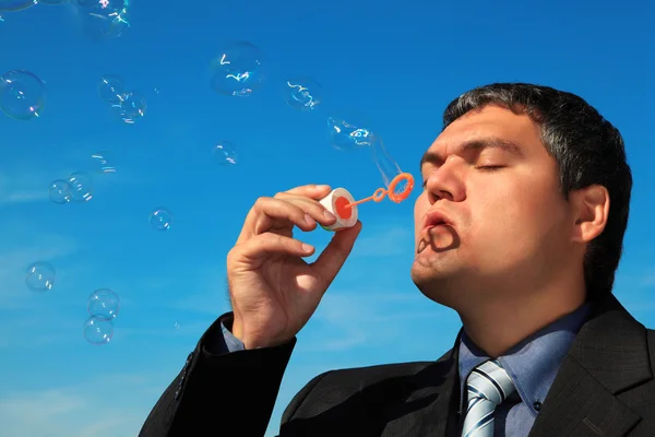 Zakenman blaast zeepbellen tegen hemel — Stockfoto