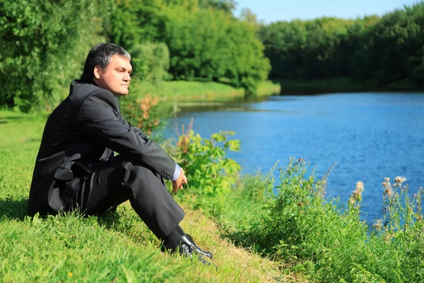 Hombre de negocios descansando sentado en la orilla del río — Foto de Stock