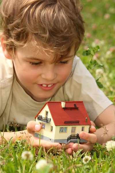 Menino encontra-se na grama com modelo de casa nas mãos — Fotografia de Stock