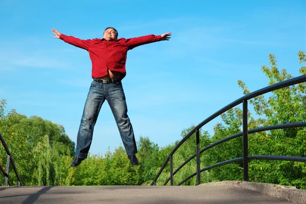Man in red shirt jumps outdoor in summer on bridge — Stock Photo, Image