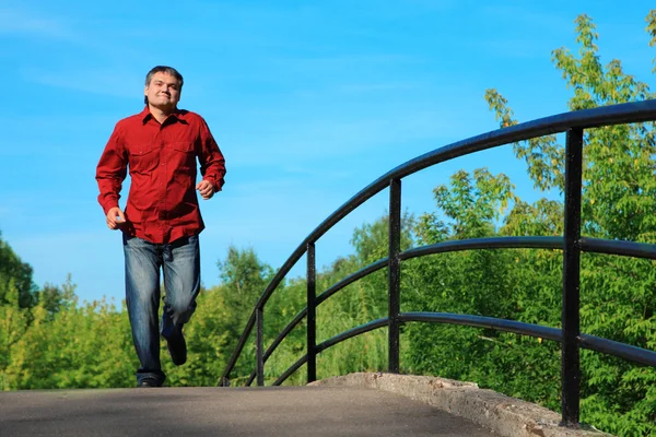 Homem de camisa vermelha corre na ponte no verão — Fotografia de Stock