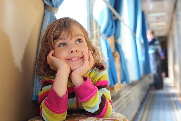 Girl sits in corridor of railway car and looks upward