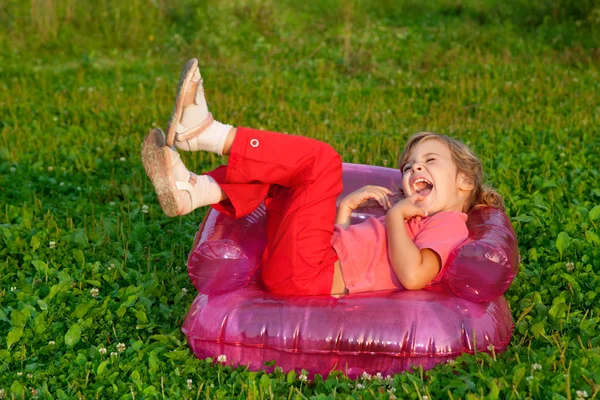 Young girl playing tricks in inflatable armchair outdoors — Stock Photo, Image