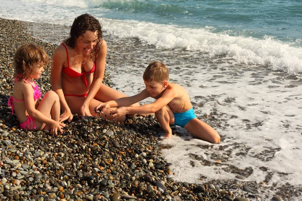 Madre con hijos se sienta en la costa — Foto de Stock