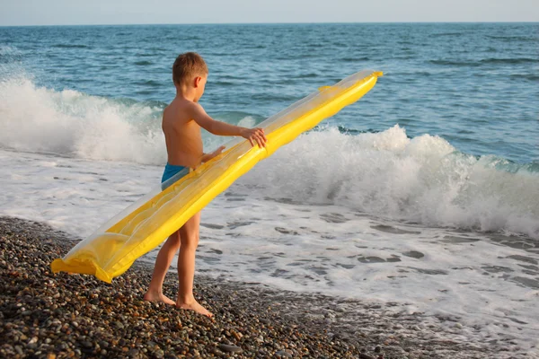 Мальчик с надувным матрасом стоит на берегу моря — стоковое фото