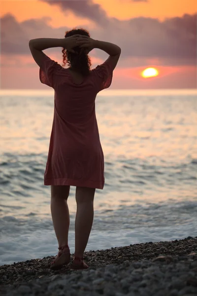 Молодая женщина стоит на берегу моря на закате, вид сзади — стоковое фото