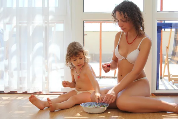 Mãe com filha sentar no chão no quarto e comer cereja — Fotografia de Stock