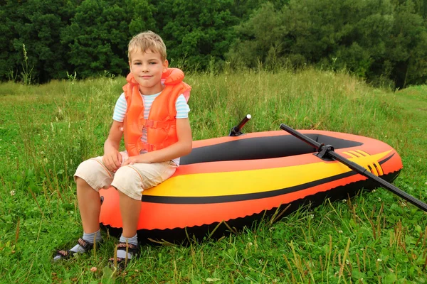 Boy sits on an inflatable boat on lawn — Stock Photo, Image