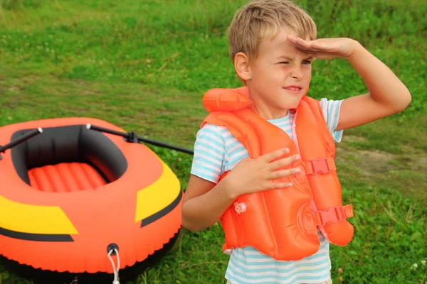Boy keeps watch and inflatable boat on lawn — Stock Photo, Image