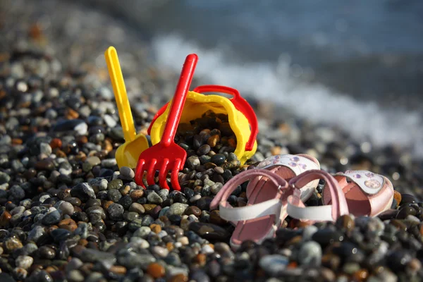 Yellow children's bucket with a scoop, a red rake and sandals on — Stock Photo, Image