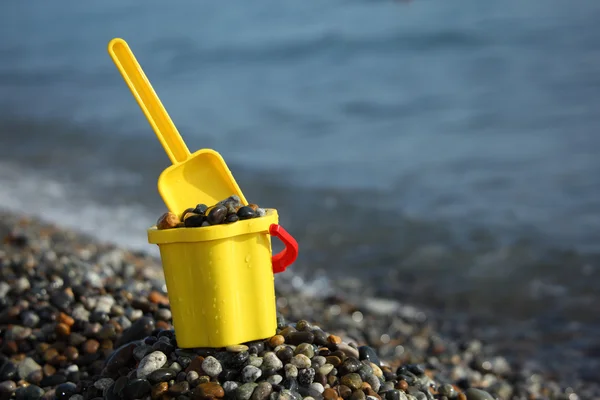 Balde infantil amarelo cheio de seixos com colher no litoral — Fotografia de Stock