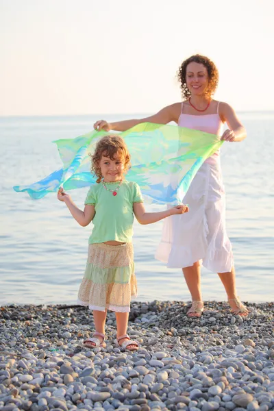 Matka s dcerou stojí na mořského pobřeží s šál v rukou — Stock fotografie