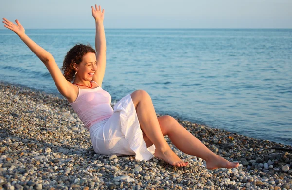 Młoda kobieta siedzi na brzeg morza z noszenia rąk — Zdjęcie stockowe